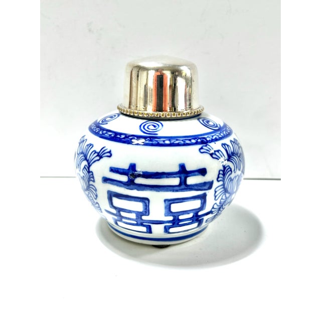 A petite vintage blue-and-white porcelain tea jar decorated with bold floral motifs and topped by a polished metal lid....