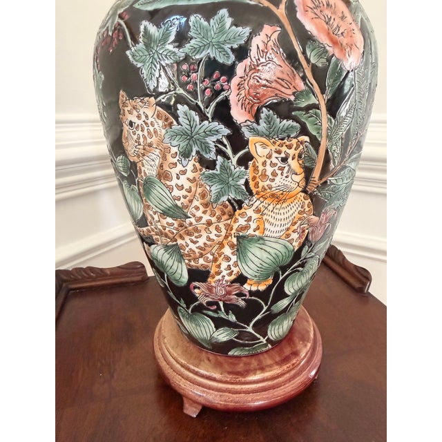 Striking vintage ceramic table lamp featuring a lush Chinoiserie-inspired leopard and botanical motif against a glossy...