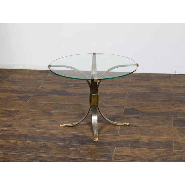 A French Art Deco period steel and brass drinks table from circa 1930, with circular glass top, four splaying legs and...