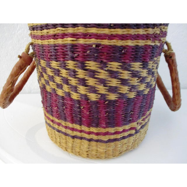 Well made African woven basket in shades of purple, magenta and tan with leather wrapped double-handles. Excellent condition.