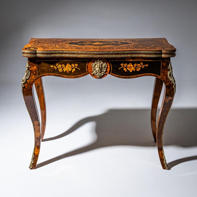 Elegant games table standing on cabriole legs, veneered in burl wood and fitted with bronze mounts in the form of rocaille...