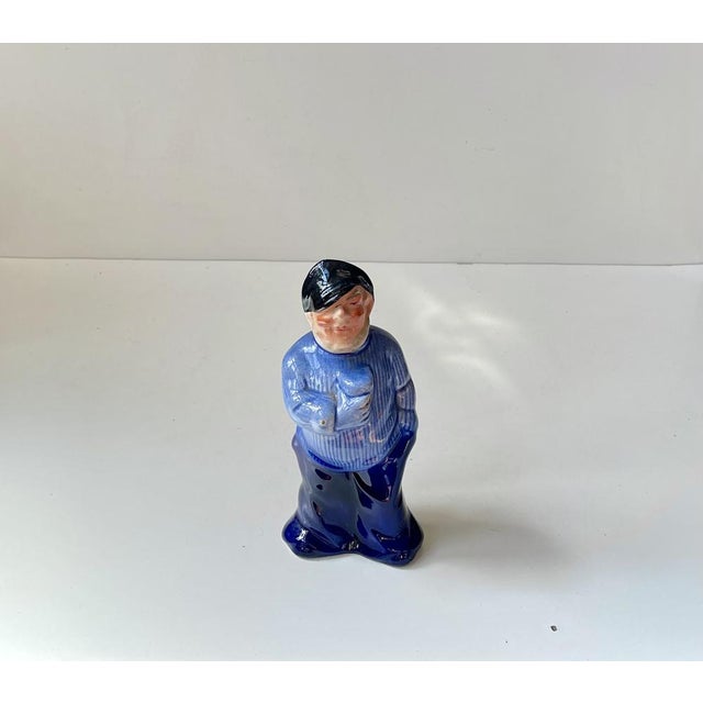 A figural decanter in hand-glazed porcelain. It depicts a jolly sailor or fisherman enjoying a cold one. Unknown...