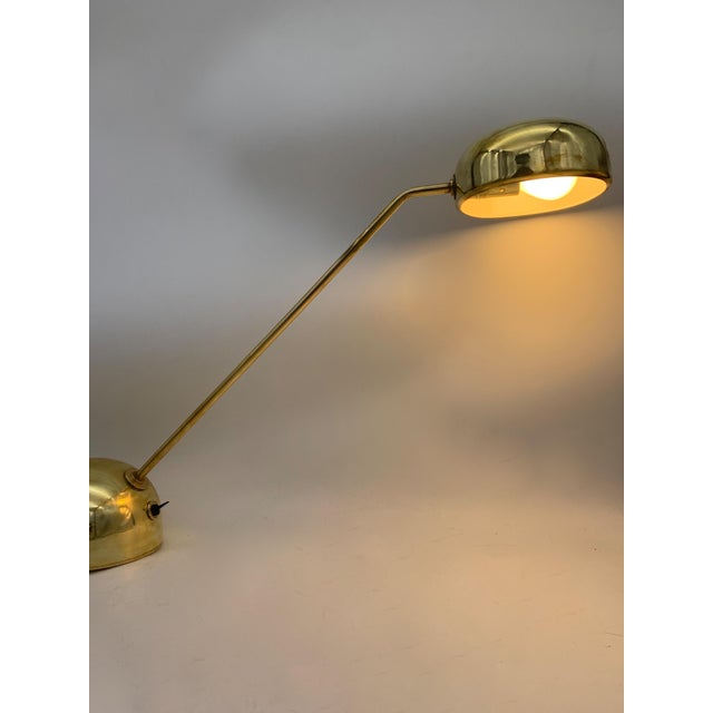 Polished brass table lamp with inclined rigid single arm structure, stable hemispherical base with integrated switch, flat...
