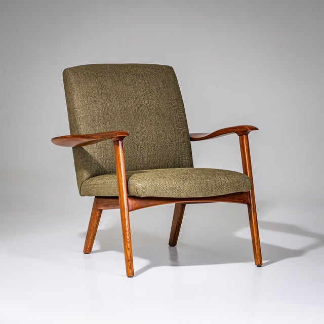 Pair of lounge chairs on finely crafted polished oak frames featuring broad, gently flattened armrests. The seats have...