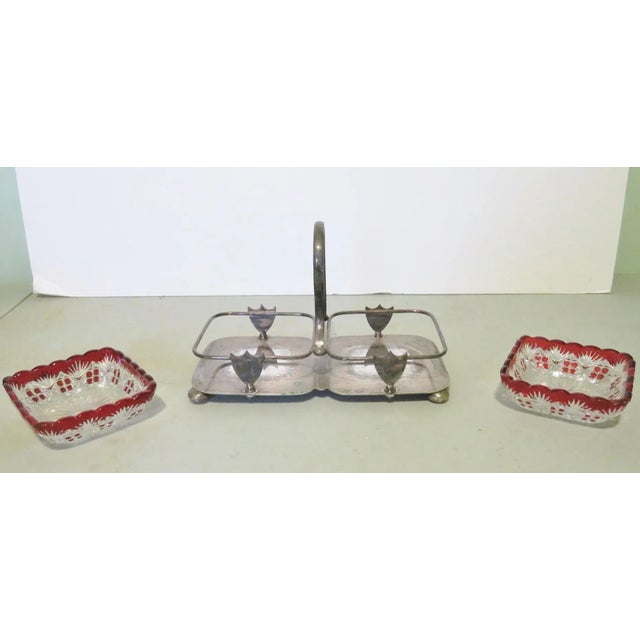 Silverplate holder with center decoration and looped handle. Two cut glass bowls with cranberry colored decoration to...