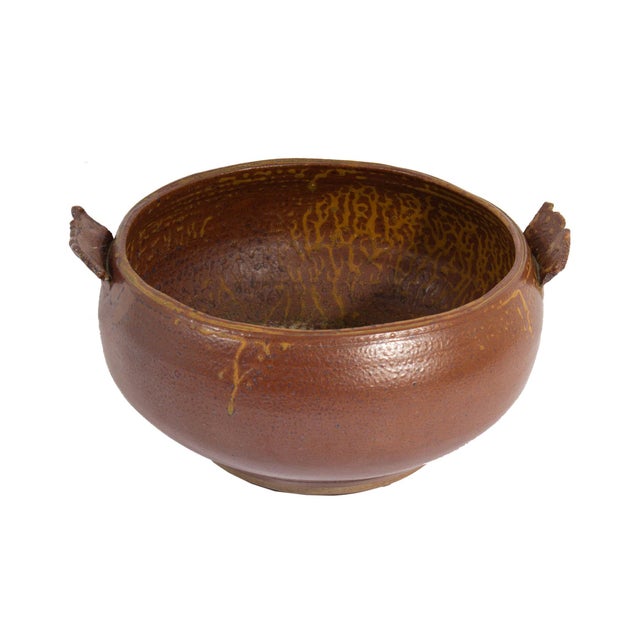 A studio pottery bowl with handle. Unsigned, this bowl exhibits a wide body which curves in to the base. The bowl's glaze...