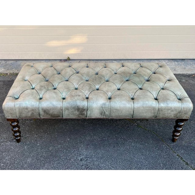George Smith ottoman in tufted leather on turned legs. The leather is an olive green color that faded to a tan/green with...