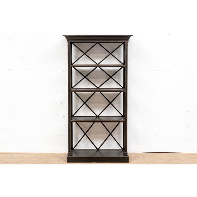 A tall, open-frame étagère or display shelf in a Hollywood Regency style and finished in ebonized black with gilt-edged...