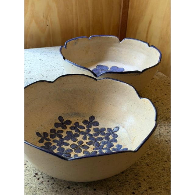A pair of hand-thrown stoneware bowls, each shaped with a distinctive scalloped, petal-like rim finished in cobalt blue....
