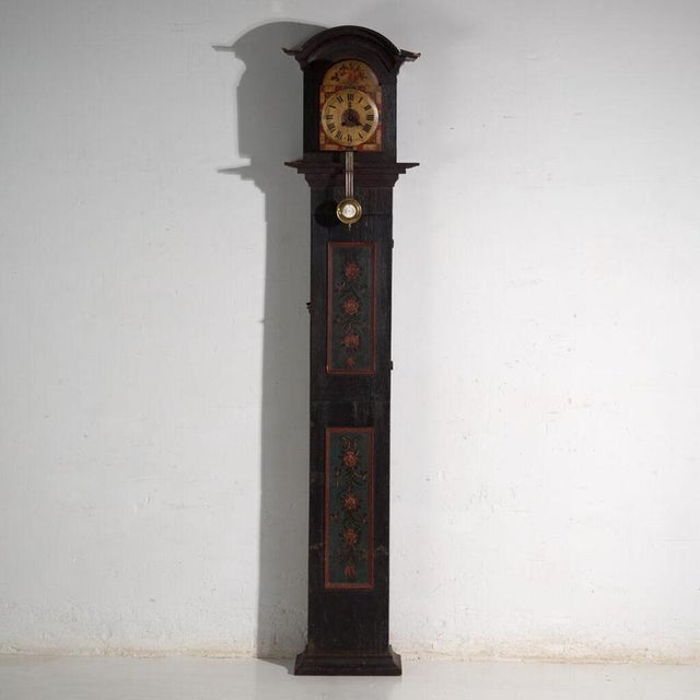 This antique longcase clock rises on a solid pine case painted in dark green, with two painted panels of floral sprays...