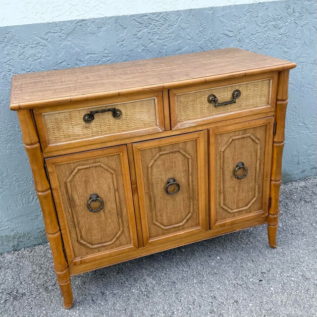 A charming Boho Chic sideboard by Broyhill featuring warm oak-toned wood, faux bamboo detailing, and woven wicker drawer...
