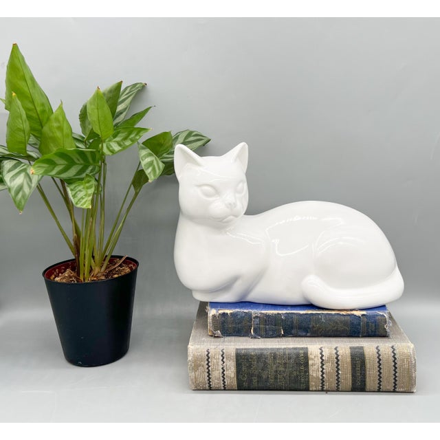 Charming ceramic cat figurine made in Holland, featuring a glossy white glaze and a relaxed reclining pose with its tail...