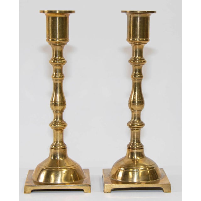 Pair of Georgian polished brass candlesticks having a shaped column raised on a square footed base. Pair of Georgian...