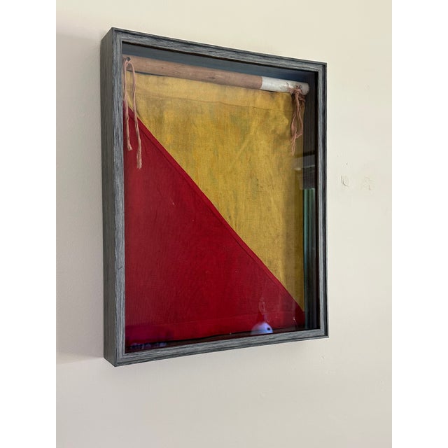 1940s era red and yellow signal flag framed in a newer gray shadow box with a portion of its original painted pole.