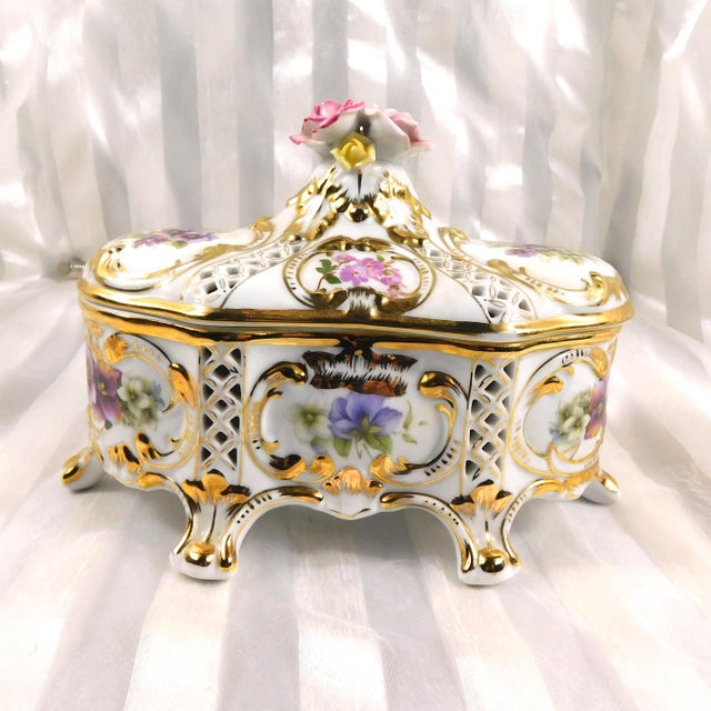 This is a KPM marked Large foooted trinket box with a matching lid. It is white with pink and purple floral designs,...