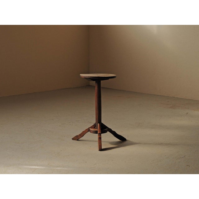 19th-century folk table in solid oak, with a thick, rounded top resting on a simple tripod base. The central column is...