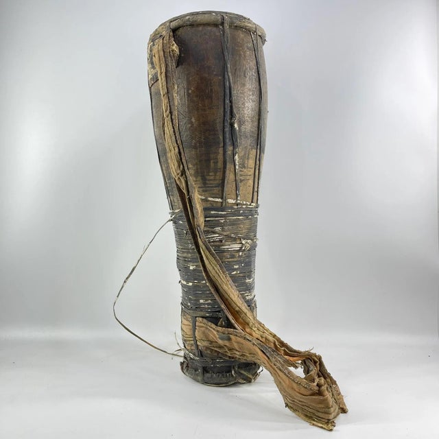 Handcrafted cylindrical drum featuring a stretched hide head, vertical rawhide tensioning, and a wrapped central grip....