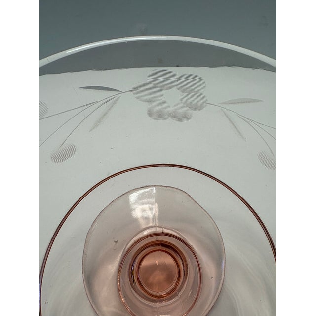Elegant vintage pink pressed glass compote featuring delicate acid-etched floral and leaf motifs. The shallow coupe form...