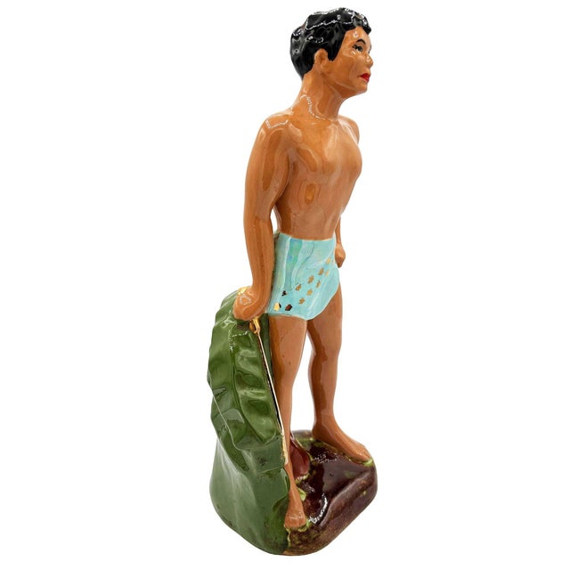 Mid-century ceramic figurines depicts a stylized Hawaiian/Polynesian man with gold machete in hand in a tropical setting ....