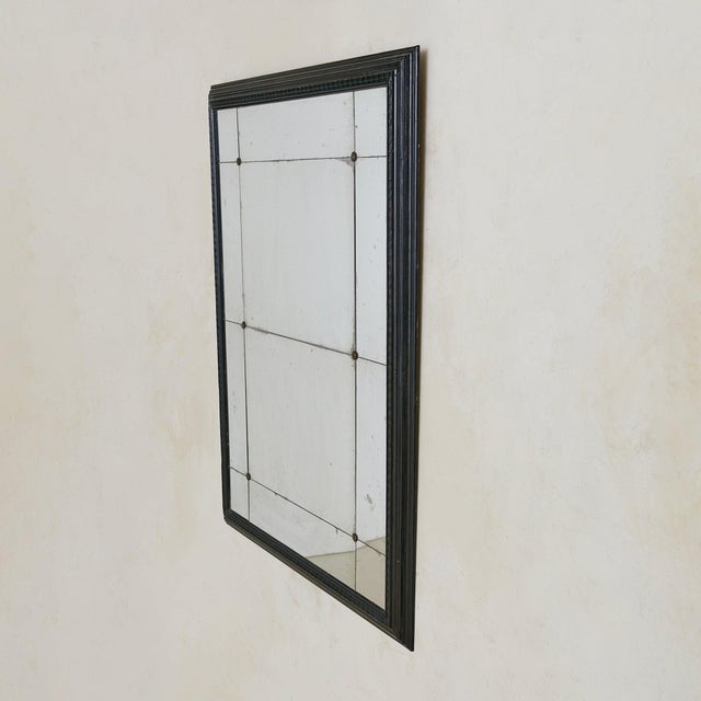 A Louis XVI style wall mirror from the 1960s, framed in carved wood finished in black lacquer. The rectangular frame is...