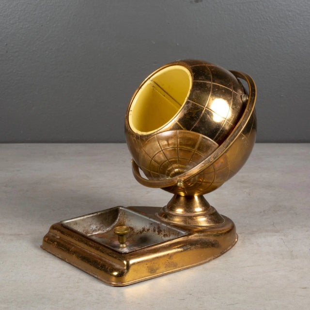 ABOUT An original mid-century brass cigarette holder with ashtray or coin dish. The lid slides open on the globe's axis to...