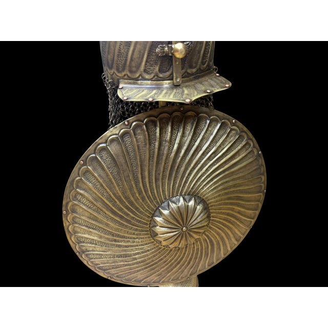 A handmade Turkish brass armor display featuring a tall domed helmet and round shield mounted on a matching pedestal...