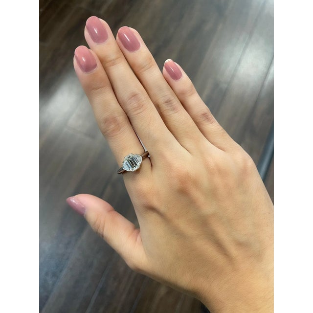 This stunning bezel set ring features a GIA certified emerald cut diamond weighing 1.23 ct. There are two cadillac cut...