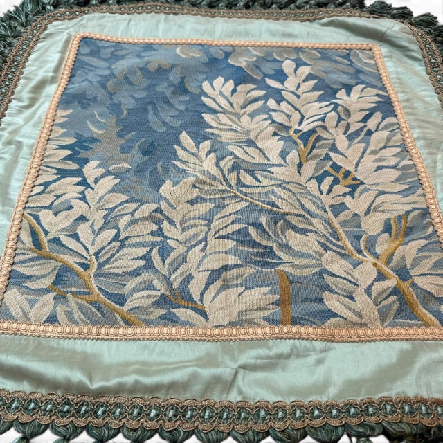 A beautifully detailed antique silk cushion cover featuring a central floral tapestry panel in soft shades of ivory and...