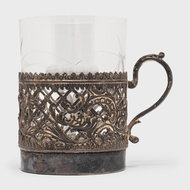 This 20th century European silver cup holder, set with a glass tumbler, boasts an exquisitely detailed filigree mount and...