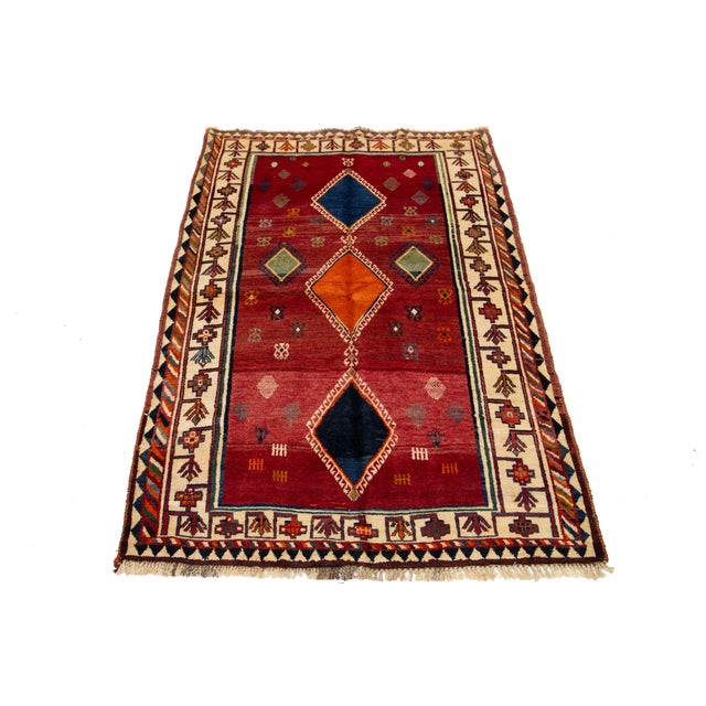 This Persian Shiraz hand-knotted wool rug has a red field with a multicolor geometric design. This rug measures 4'5" x 7'2".