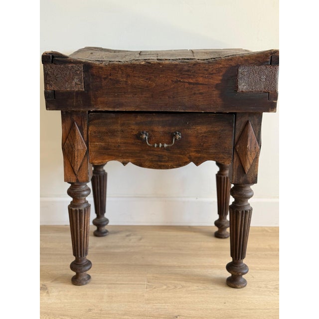 A dark, heavy French butcher block table — the thick plank top banded at each corner with iron strapping secured by hand-...