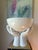 Striking Italian ceramic centerpiece featuring a large white bowl cradled by a sculptural pair of hands. The glossy white...