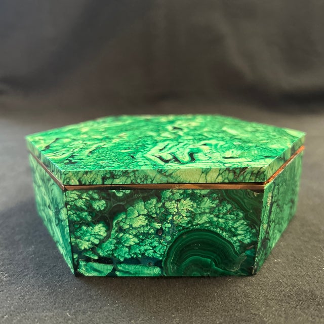 Solid malachite covered accessories box. It has brass and wood borders between the lid and the base. The coloration is...