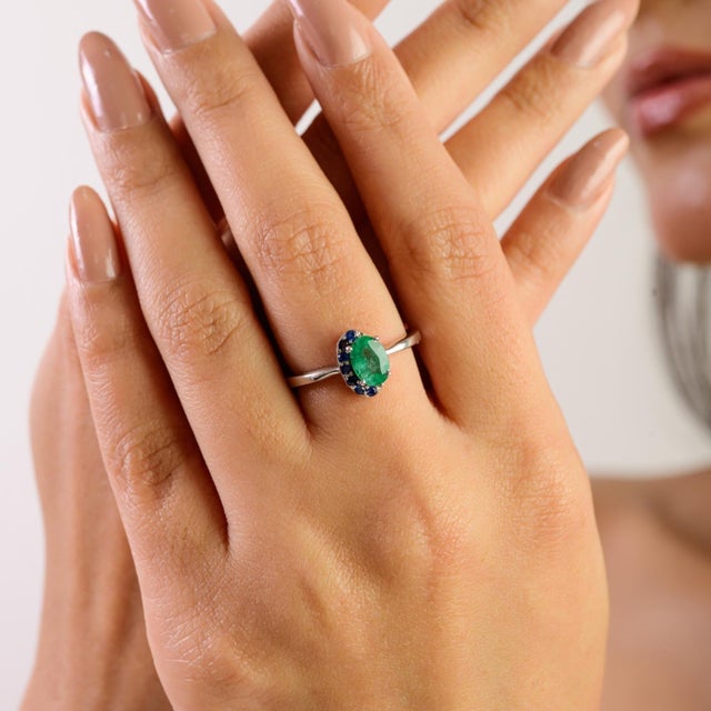 Crafted in 925 sterling silver, this minimalist ring features a stunning 7x5 mm oval emerald paired with a 1.5 mm round...
