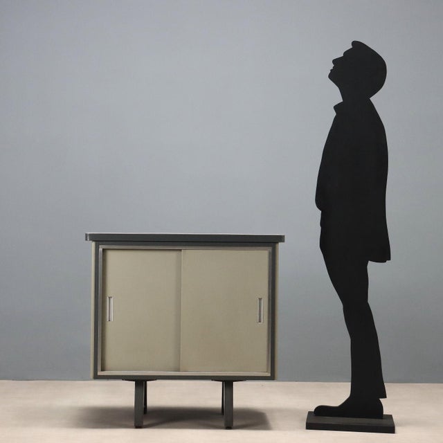 Vintage storage unit made of lacquered metal with sliding doors. This piece is attributed to the mentioned designer/maker....