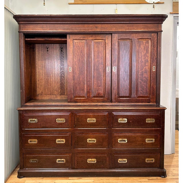 Antique storage cabinet made of dark stained quarter sawn oak with recessed brass hardware. It features nine dovetail...