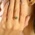 This minimalist three-stone ring showcases a natural oval-cut emerald weighing approximately 0.37 carats, set in solid 14K...