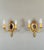 An elegant pair of gilt bronze wall sconces, each adorned with an oval beveled mirror. The two candle-shaped arms evoke...