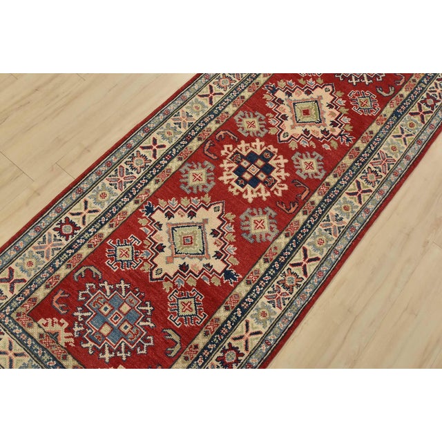 A tribal Caucasian Kazak runner hand-knotted with fine wool on a cotton foundation. This rug features geometric medallions...