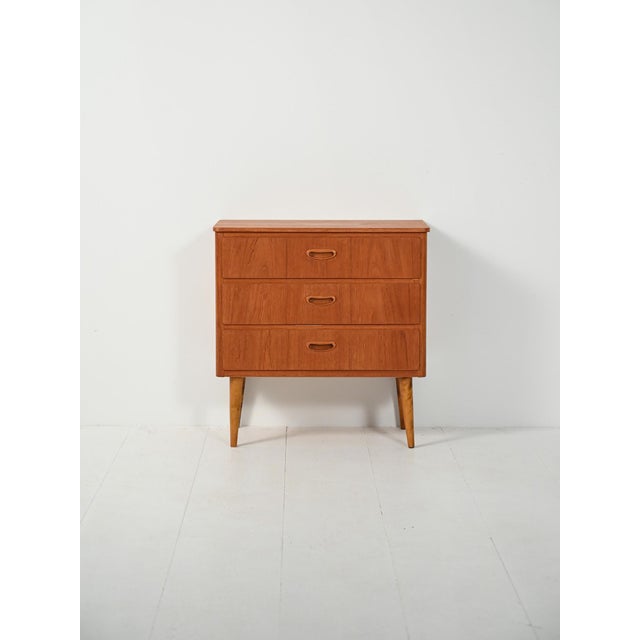 Small Scandinavian chest of drawers from the 1950s in teak with turned birch legs. Three drawers with recessed carved...