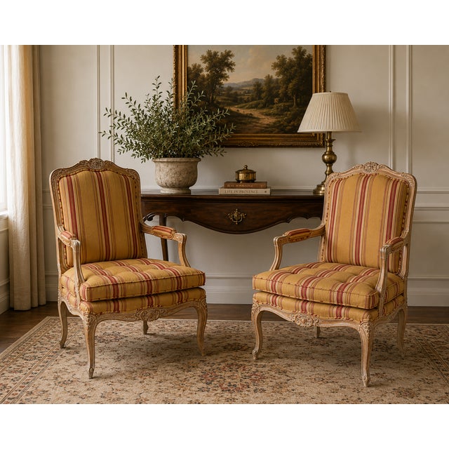 A charming pair of Louis XV style bergere armchairs featuring carved frames, cabriole legs, and warm striped upholstery in...