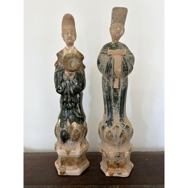 Statues of a Chinese man and woman crafted from terracotta, featuring green and umber glazes. The wide-sleeved robes and...