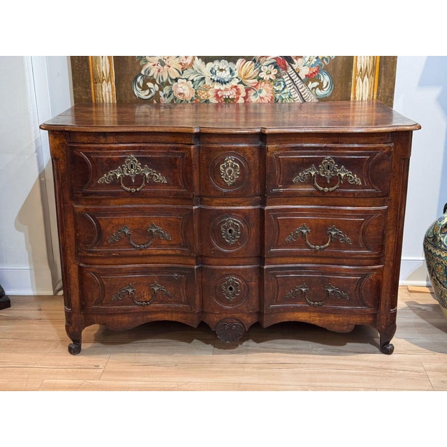 Early 18th C. French Provincial walnut commode with a shaped, molded top over a serpentine front. Three long drawers have...