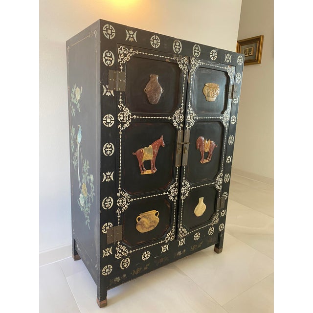 Beautiful antique black Chinoiserie cabinet adorned with hand-painted decorative shells and designs of various pots and...