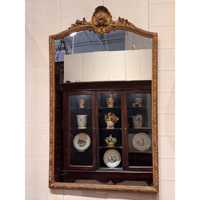 19th century French giltwood mirror with an arched top crowned by a carved shell crest flanked by scrolls and flowers. The...
