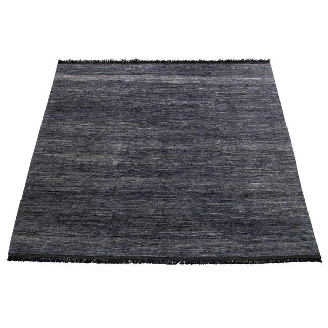 This handcrafted wool rug, designed in the Gabbeh style, features a solid design highlighted by black fringes and a gray-...
