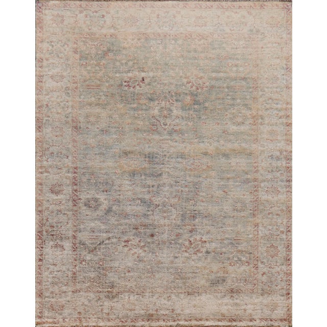 A revival handwoven Oushak from Pakistan. This decorative piece features a light blue background with mauve accent color...