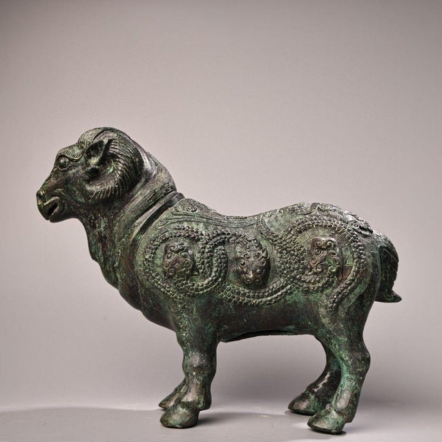 This striking antique bronze sculpture depicts a standing ram, a traditional symbol of strength, prosperity, and filial...