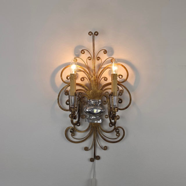 The lamp features flowing tendrils and ornamental curls in gilded metal. A silvered crystal glass element sits at its...