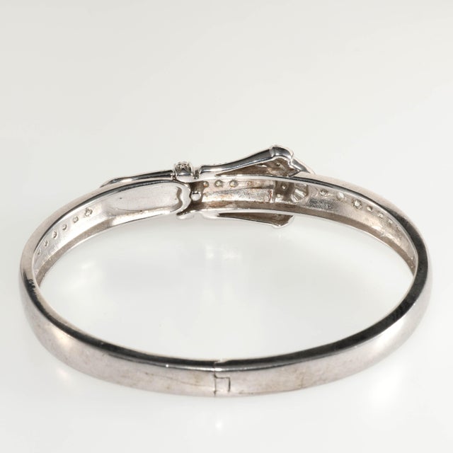 Hinged bangle crafted of sterling silver metal in a style imitating antique buckle bracelets. Finely crafted with bead set...